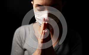 Sick young woman in protective face mask praying