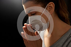 Sick young woman in protective face mask praying