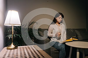 Sick young woman is reading a book in a dark room.