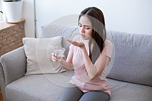 Sick young woman taking pills while sitting on the sofa at home