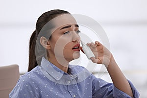 Sick young woman using nasal spray in office