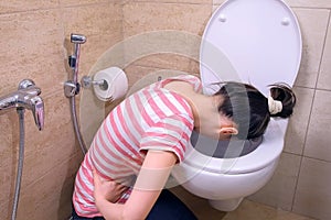 Sick young woman is vomiting in toilet sitting on the floor at home, food poisoning symptom.