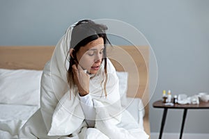 Sick young woman wrapped suffering from cold symptoms at home