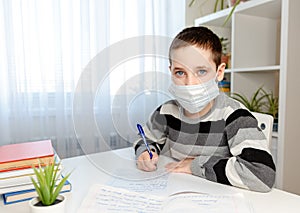 Sickness boy in medical mask studying at home and doing homework photo