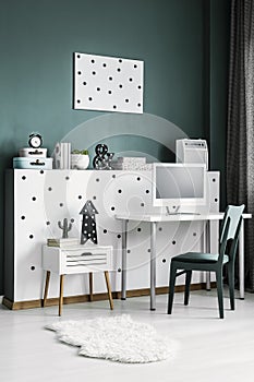 Side angle of an elegant home office interior with a desk, computer, chair, cabinet and dotted wall