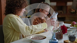 Side angle view loving brother pouring milk in morning cereal of sister and own bowl. Happy positive cheerful Caucasian