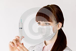 Side angle view of young Caucasian nurse or doctor woman wearing medical face mask and white coat, holding syringe with