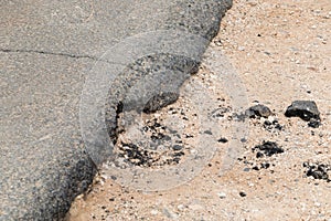 A side of an asphalt road with a piece of crumbled asphalt close-up. Concept of wear and tear of the road surface