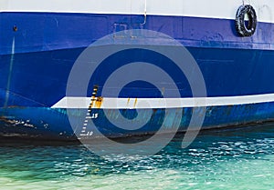 Side of blue cargo ship hull with white waterline and numbers of rough draft scale. International load line, Plimsoll line or