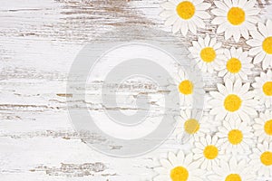 Side border of white daisy flower paper decorations over a rustic white wood background