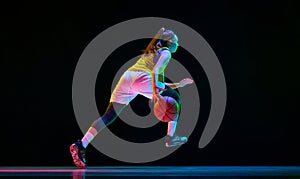 Side bottom view image of young girl, basketball player in motion, running with ball against black studio background in