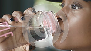 Side close-up portrait of the young attractive african girl drinking water via the plastic bottle.