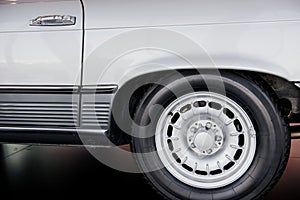 Side close up view of white retro car with white light alloy wheel and low-profile tire, chrome disk, arch above