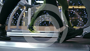 Side closeup view of a feet of a unrecognizable sportpeople in motion walking on treadmills in the gym warming up before