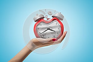 Side closeup of woman`s hand facing up and holding damaged retro alarm clock on light blue gradient background.