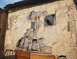 Side facade of an old rotten abandoned building with broken windows and peeling stucco