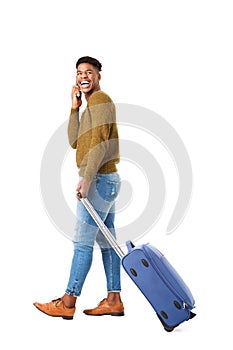 Side of happy young african american travel man walking with mobile phone and suitcase against isolated white background