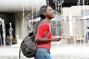 Side of happy young black woman walking in the city with bag and smart phone