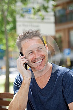Side of laughing man sitting on park bench with cellphone
