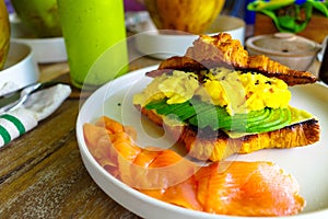 A side look of healthy food - croissant with scramble eggs, sliced avocado, smoked salmons.