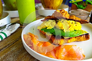 A side look of healthy food - croissant with scramble eggs, sliced avocado, smoked salmons. photo