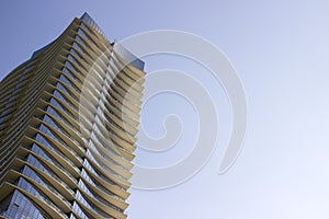 Side low angle view of a modern corporate high-rise office building with yellowish overhangs in each floor.