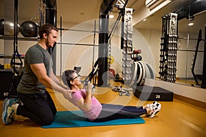 Side of male trainer helping middle aged woman doing sport exercise for back