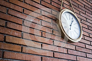 Side medium shot of a wooden wall clock with roman numerals hanging in a red brick wall.