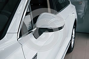 Side mirror. Particle view of modern luxury white car parked indoors at daytime
