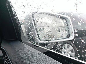 Side mirror with the rain drops rolling on window on the road with traffic jam in the rainy day.