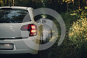 Side mirror turn signal blinker. Turn indicator on the mirror right and white car on the road in autumn dark forest.