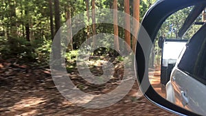 Side mirror view reflection of car and caravan driving in a forest during road trip in Australia