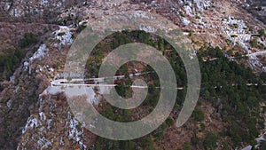 Side panoramic view of extreme serpentine road on slope of mountain covered with sparse vegetation, Montenegro, drone