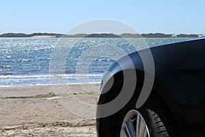 Side part of a black car parked on the beach in front of the ocean