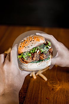 Side of a person holding a half-eaten hamburger with cheese, lettuce, tomato, onion, and french fries