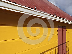 Side perspective view of yellow wooden facade, closed shutter and Caribbean tin roof. Tropical architecture and construction.