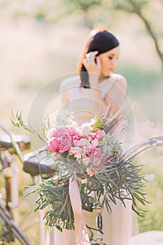 The side photo of the blurred bride holding her dark hair in the white wedding dress near the blurred bicycle with the