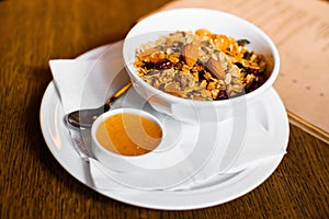The side photo of the cereal with nuts and raisins placed near the little dish with honey.