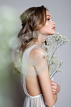 Side photo of a very beautiful young model in bridal dress with gypsophila flowers in her hands. Romantic style.