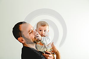 Side portrait of adorable baby in his father`s arms touching his face with his little hands, white background