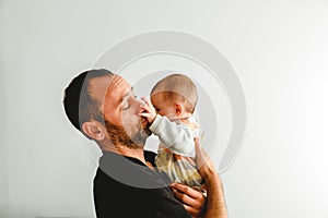 Side portrait of adorable baby in his father`s arms touching his face with his little hands, white background