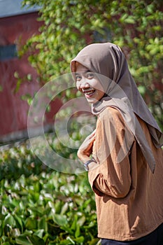 side portrait of a beautiful woman wearing a modern hijab in a garden with a sweet smile and left hand on her chest