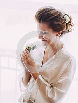 The side portrait of the bride in the silk robe holding the mini-bouquet consisted of white roses.