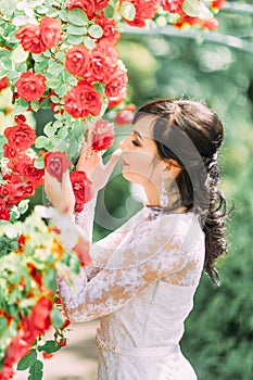 The side portrait of the bride touching and smelling red roses.