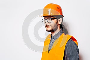 Side portrait of construction engineer in orange vest, wearing hardhat on white