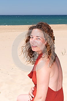 Side portrait of curly brunette forties woman in sand ocean beach