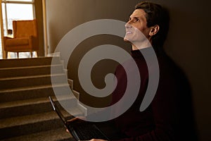 Side portrait of a handsome man working remotely on laptop against dark brown wall background. Businessman, entrepreneur,