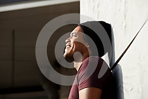 Side portrait of handsome young african american man leaning against wall and smiling