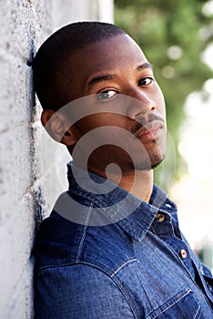 Side portrait of handsome young black man leaning on wall outside