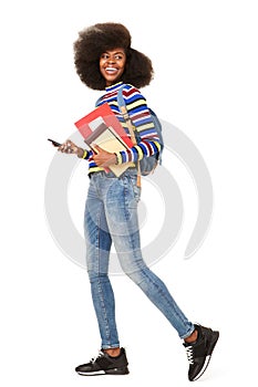 Side portrait of happy young black woman walking with cellphone and book bag